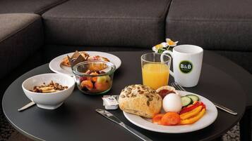 Ein Frühstückstisch mit einer Schüssel Müsli, einem Glas Orangensaft, einem Teller mit Eiern, Gemüse und einem Muffin.