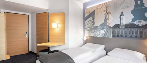 A hotel room with two beds, a desk, and a wall-mounted light.