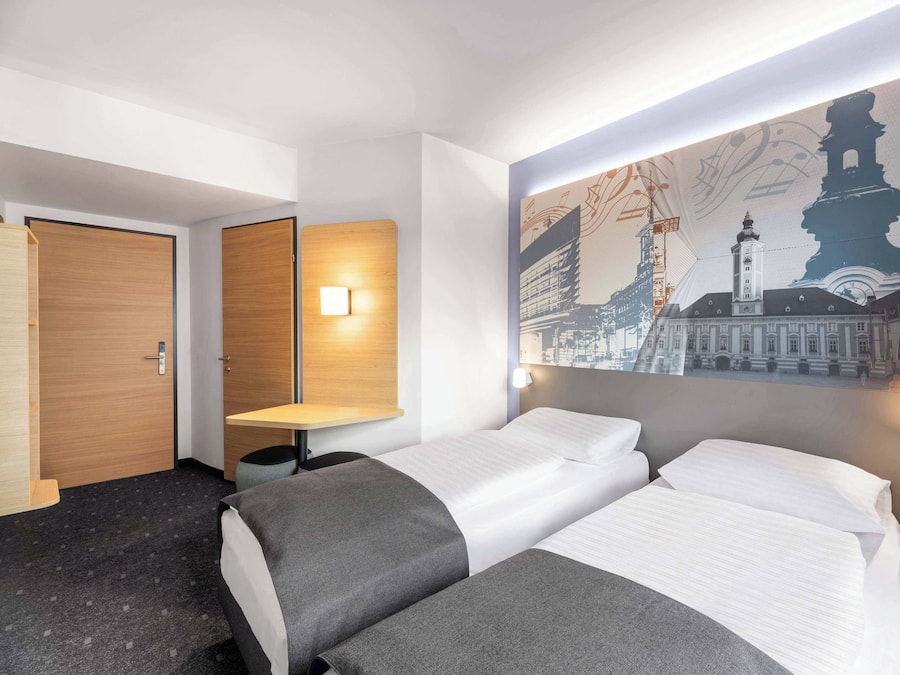 A hotel room with two beds, a desk, and a wall-mounted light.
