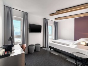 A modern hotel room with a bed, a desk with a coffee maker, a TV, and a view of the city. - B&B HOTEL St. Pölten (St. Pölten)