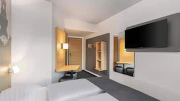 Habitación de hotel con cama, televisor montado en la pared, escritorio con silla y armario.