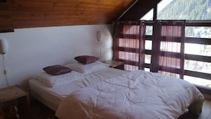 Un dormitorio con techo de madera, una cama con ropa de cama blanca, dos mesitas de noche y una ventana con cortinas.