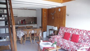 Una sala de estar acogedora con un sofá estampado, una mesa de comedor de madera y sillas. Se ve una escalera al fondo que conduce a un nivel superior.