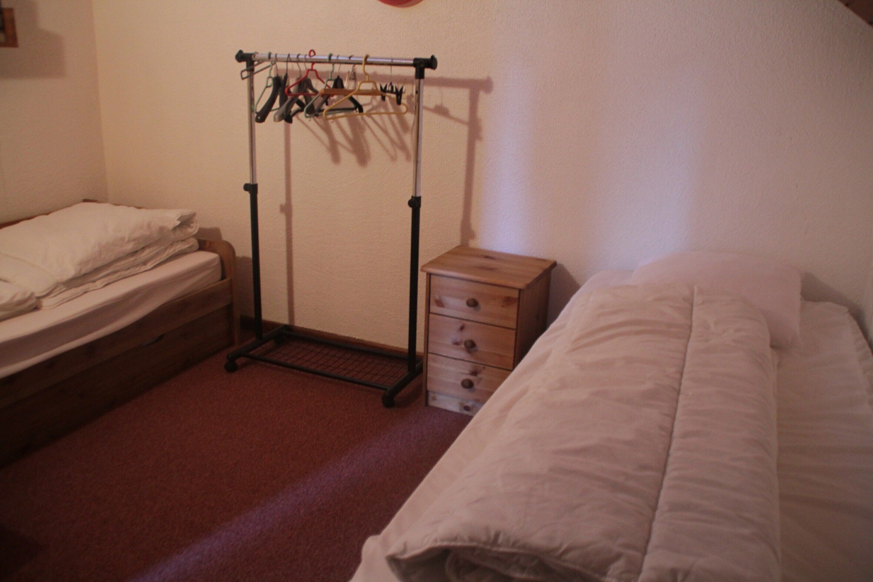 A bedroom with a bed, a small dresser, and a clothing rack.