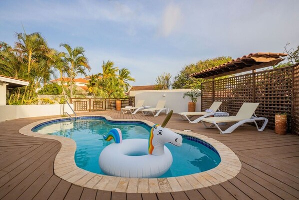 Relax by the circular pool surrounded by a wooden deck and lounge chairs, with a shaded area under a pergola.