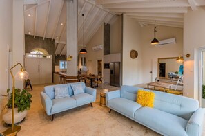Relax in this spacious living area with a sofa, coffee table, and floor lamp, surrounded by a high ceiling and large window.
