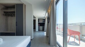 Une chambre d’hôtel avec un lit, une armoire, un coin cuisine et un balcon avec une chaise rouge.