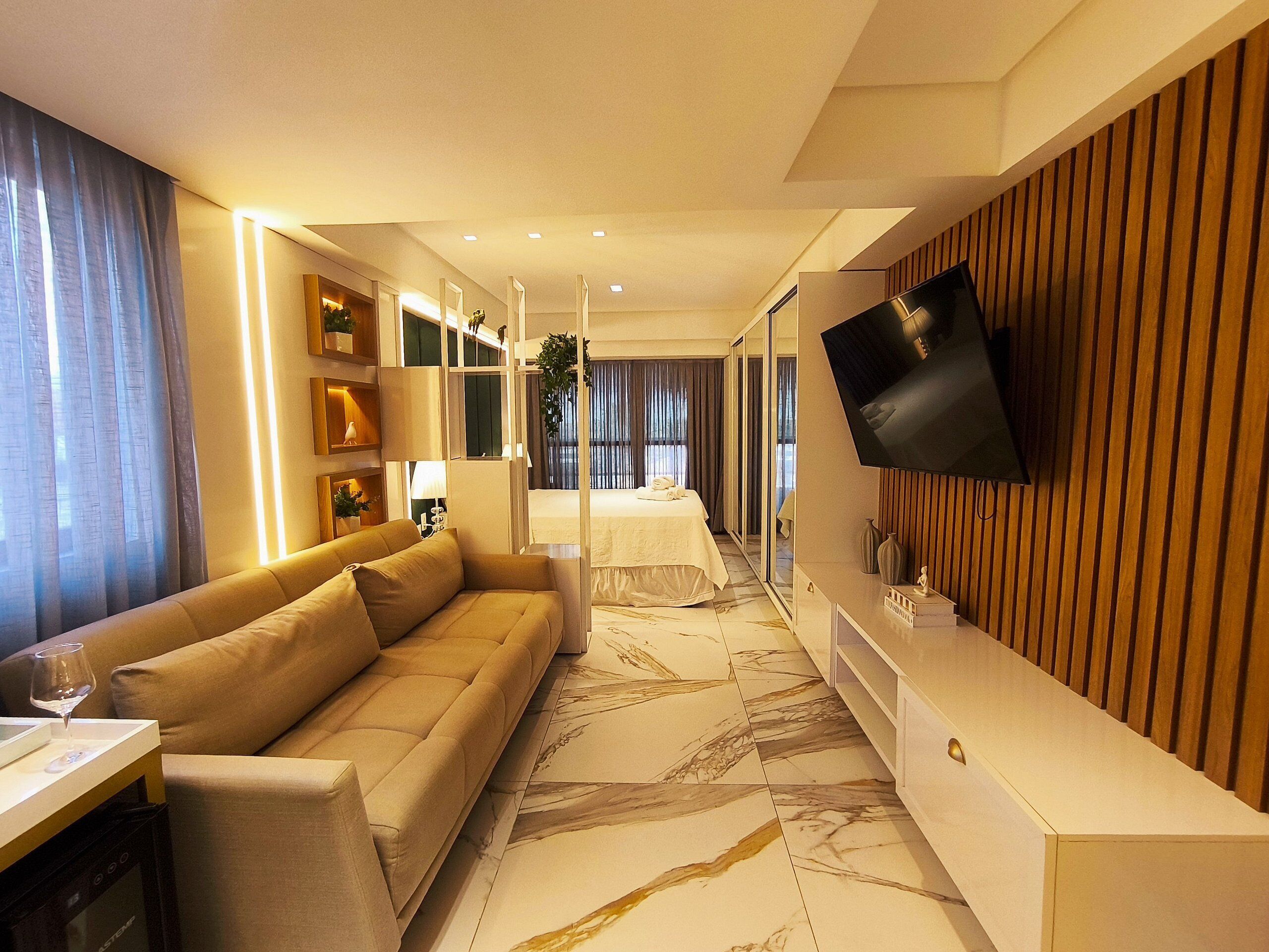 A modern hotel room with a sofa, a flat-screen TV, a dining area, and a large mirror.
