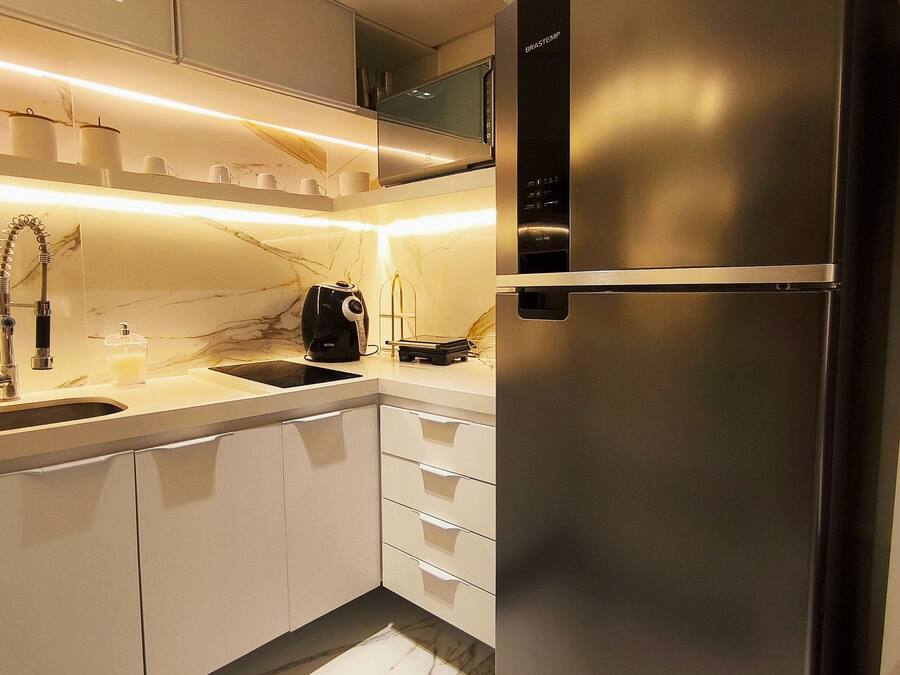 Eine moderne Küche mit einem Edelstahlkühlschrank, weißen Schränken, einer Marmorarbeitsplatte und Beleuchtung unter den Schränken.