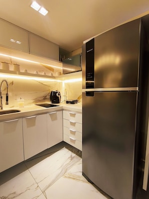 A modern kitchen with a stainless steel refrigerator, white cabinets, a marble countertop, and under-cabinet lighting.