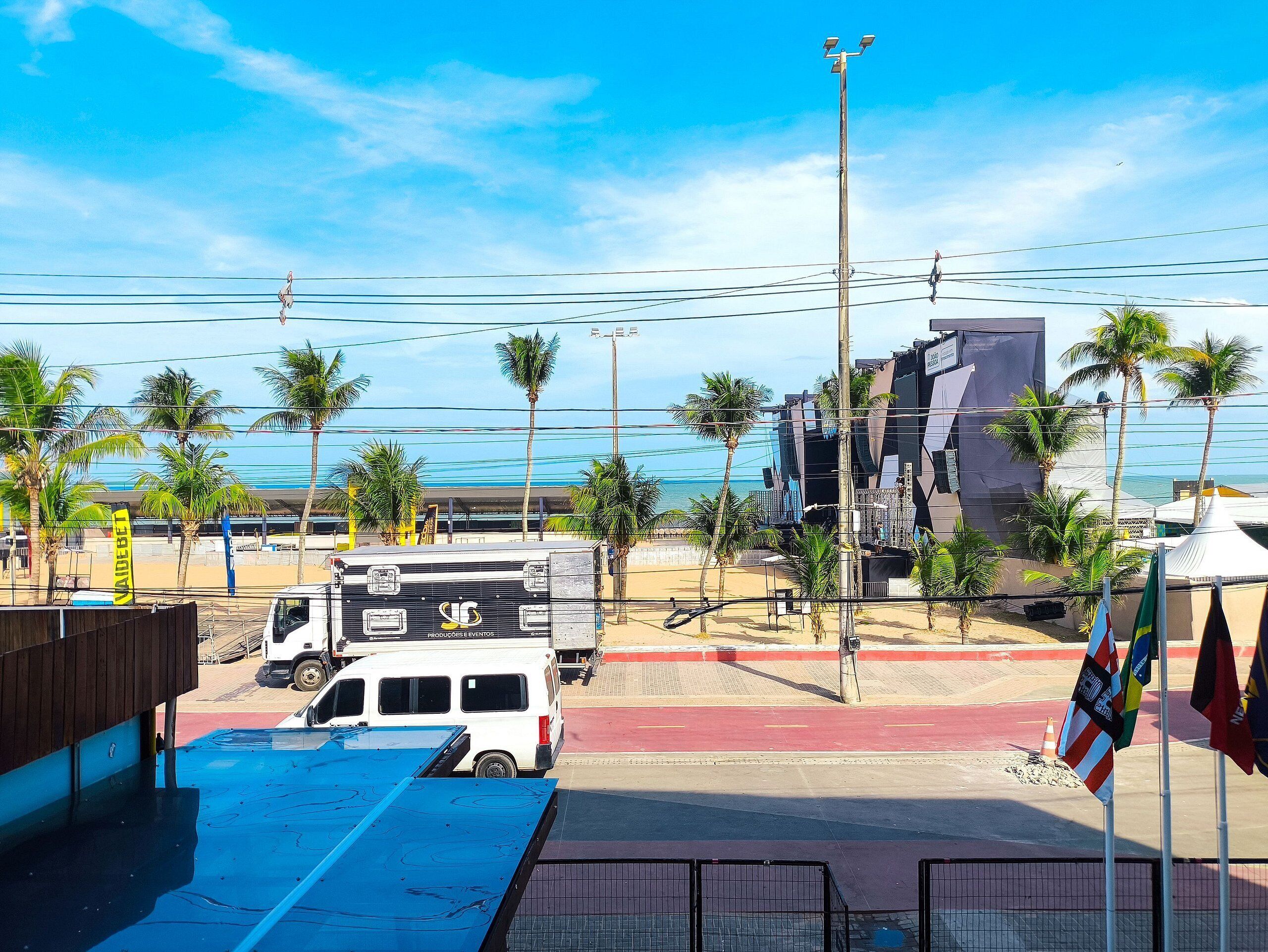 Vista de la playa con un área de estacionamiento, una camioneta blanca y un edificio con un letrero grande.