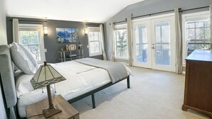 Et soveværelse med seng, natbord, lampe, kommode, et billede på væggen og en skydedør, der fører til en balkon.