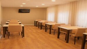 Ein Konferenzraum mit mehreren Tischen und Stühlen, einem an der Wand montierten Flachbildfernseher und einem Fenster mit Vorhängen.