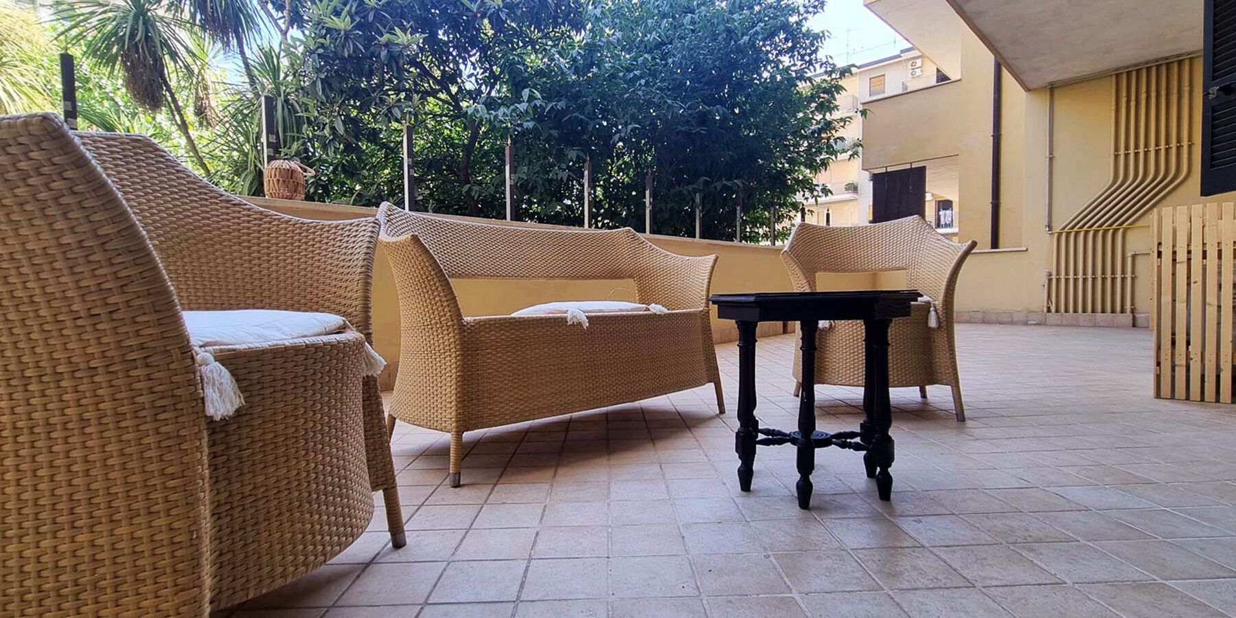 Un patio con mobiliario de mimbre, una mesa negra y un piso de baldosas.