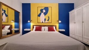 Una habitación de hotel con una cama grande, un armario, una mesita de noche con lámpara y un espejo.