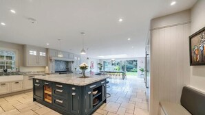A spacious kitchen with a large island, modern cabinetry, and a view to a patio area. - Legoland Basecamp | Perfect for Families | Sleeps 15 (Windsor)