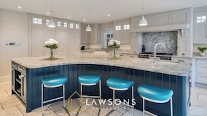 A modern kitchen with a curved island, bar stools, pendant lighting, and a marble backsplash. - Legoland Basecamp | Perfect for Families | Sleeps 15 (Windsor)
