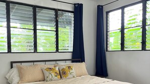 A bedroom with a bed, a ceiling fan, and windows with blinds.