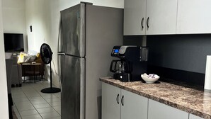 A modern kitchen with grey cabinets, a stainless steel refrigerator, a coffee maker, and a fan.