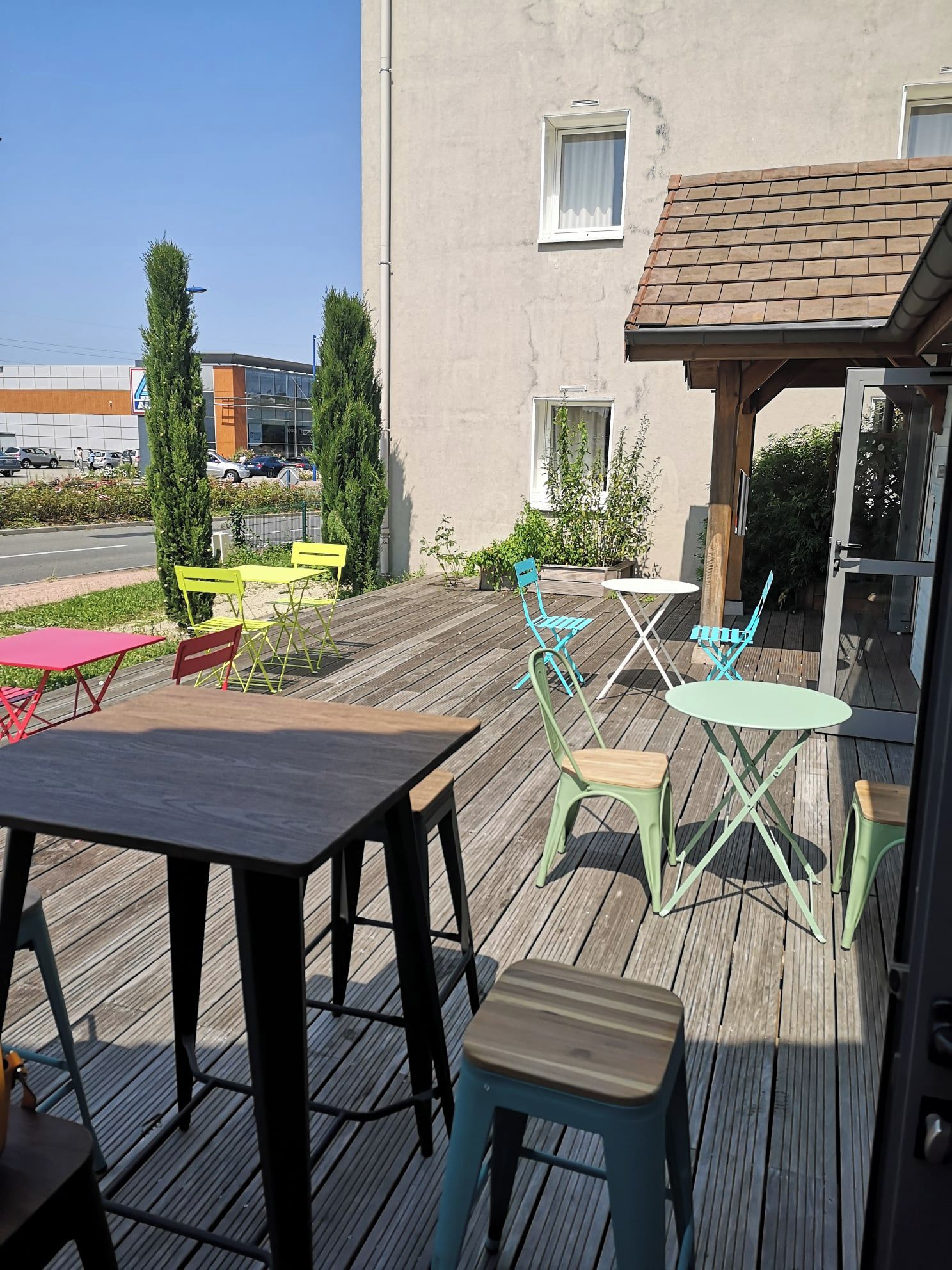 Une terrasse extérieure avec une plateforme en bois, des sièges d’extérieur et un bâtiment en arrière-plan.