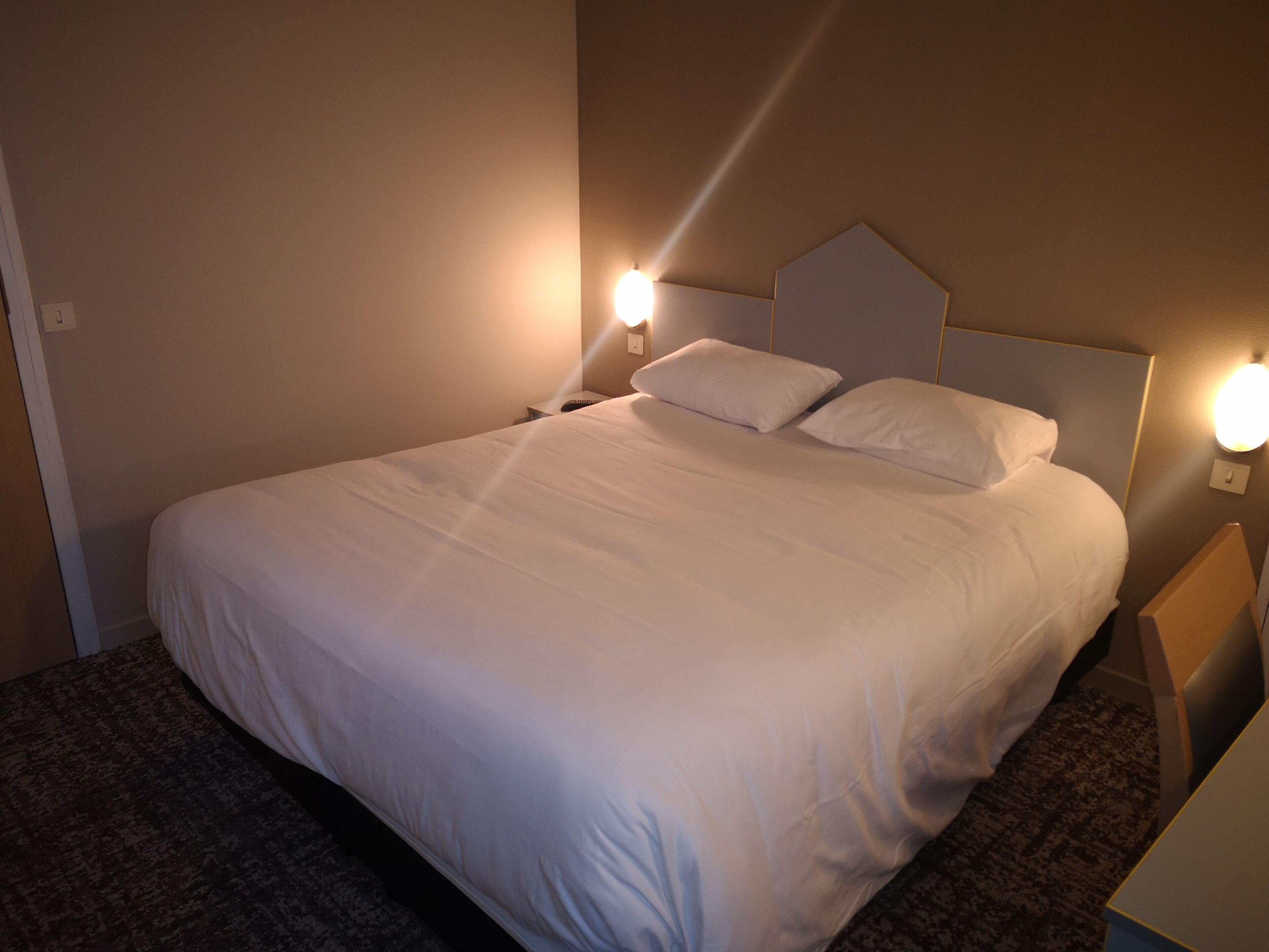 Una cama bien hecha con sábanas blancas, dos lámparas de noche y un cabecero.