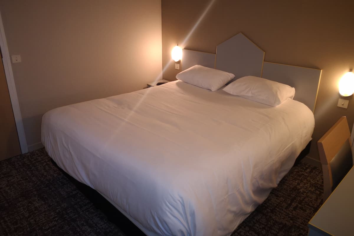 A neatly made bed with white linens, two bedside lamps, and a headboard.