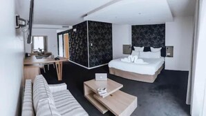 Moderni hotellihuone, jossa on sänky, työpöytä, kannettava tietokone, sohva ja sohvapöytä.