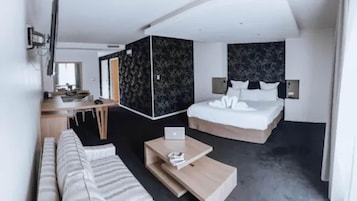 A modern hotel room with a bed, a desk, a laptop, a sofa, and a coffee table.
