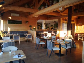 A wooden interior with tables and chairs, a bar area, and hanging plants.