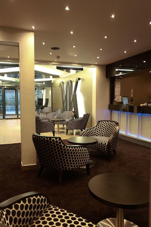 A modern lounge area with patterned furniture, a reception desk, and recessed lighting.