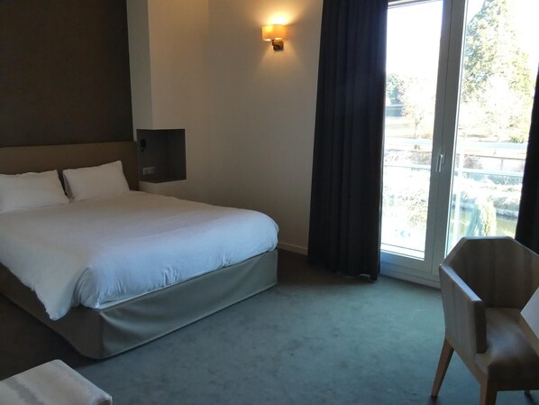 Une chambre d’hôtel avec un lit, une chaise, une lampe fixée au mur et une vue par la fenêtre.