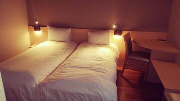 A double bed with white linens, two bedside tables with lamps, a small desk, and a chair.