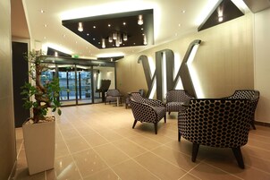 A lobby with a reception desk, patterned chairs, a potted plant, and a large wall sculpture.