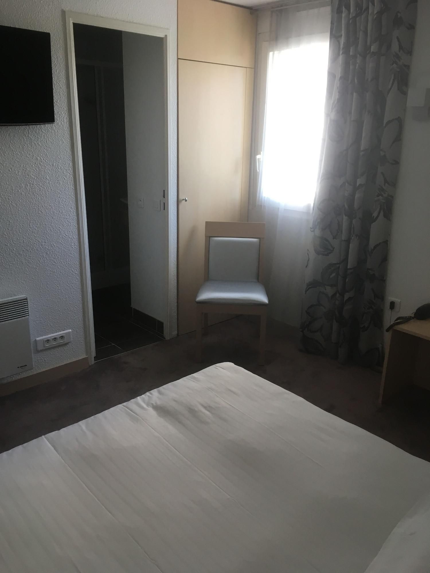 Een kamer met een bed, een stoel, een kledingkast en een raam met gordijnen.