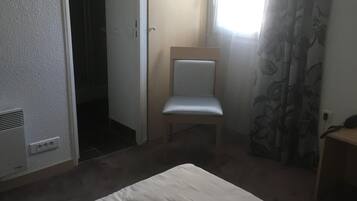 Een kamer met een bed, een stoel, een kledingkast en een raam met gordijnen.