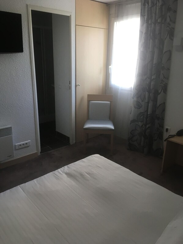 A room with a bed, a chair, a wardrobe, and a window with curtains.