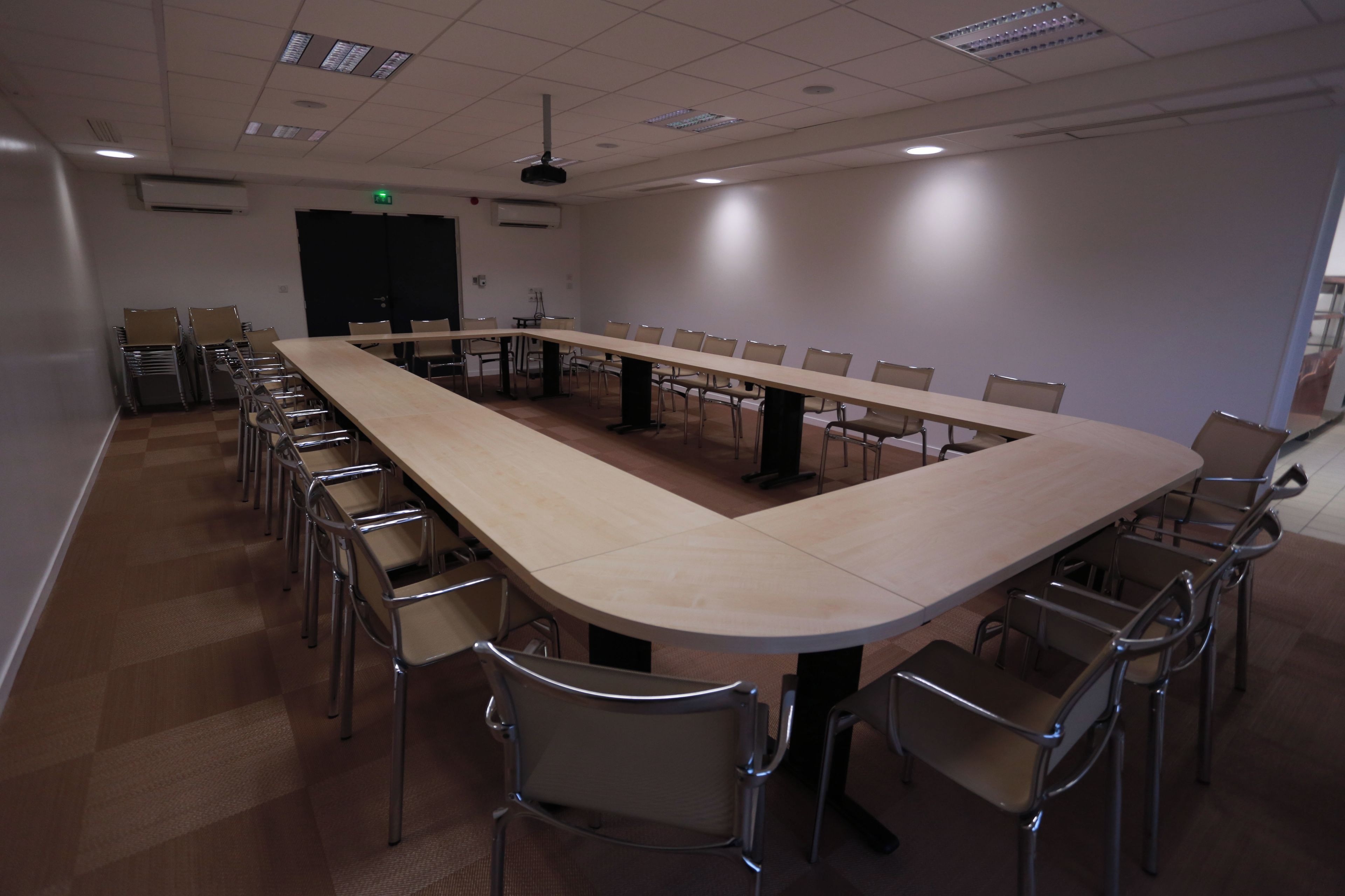 Une salle de conférence avec une longue table, des chaises et un ventilateur de plafond.