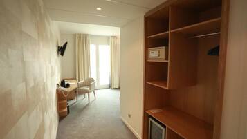 A hotel room with a wooden wardrobe, a desk with a telephone, a chair, and a television.