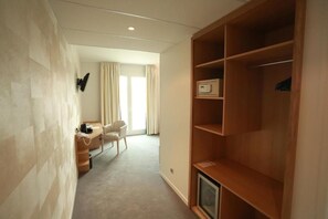 A hotel room with a wooden wardrobe, a desk with a telephone, a chair, and a television.