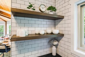 A kitchen with white subway tiles, wooden shelves, and a clock.