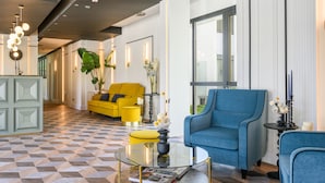 A modern hotel lobby with a checkered floor, a yellow sofa, a blue armchair, and a glass coffee table.