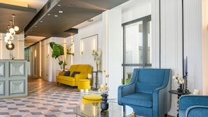 Un moderno vestíbulo de hotel con piso a cuadros, un sofá amarillo, un sillón azul y una mesa de centro de vidrio.