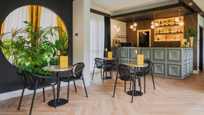 Un área de bar moderna con mesas redondas, sillas negras y una barra verde.