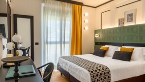 A hotel room with a bed, a desk with a lamp, a chair, and a window with curtains.