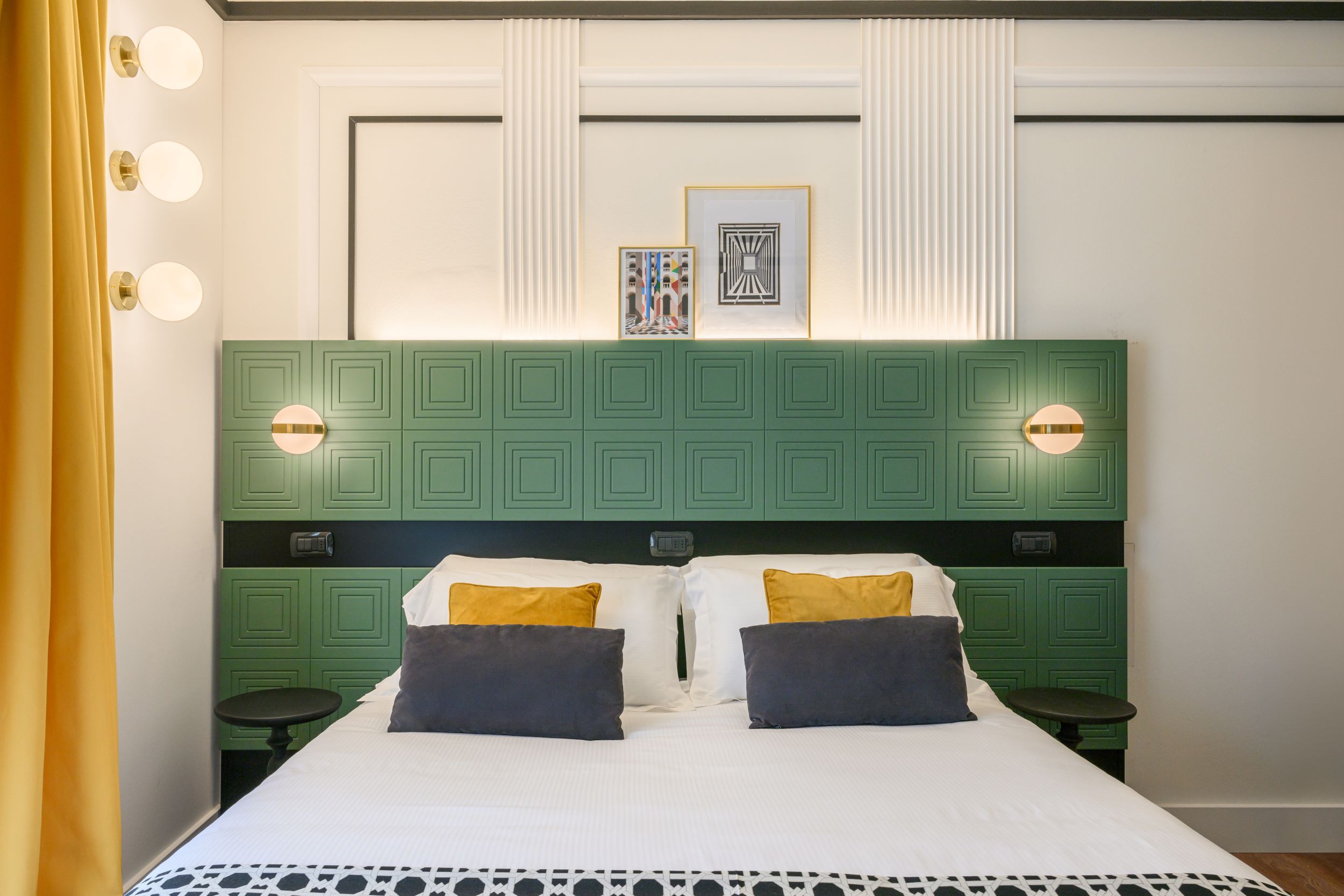 Een bed met een groen hoofdeinde, twee nachtkastjes en wandlampen.