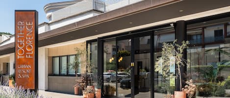 Un complexe hôtelier urbain doté d’une grande entrée en verre, de plantes en pot et d’une enseigne bien visible.