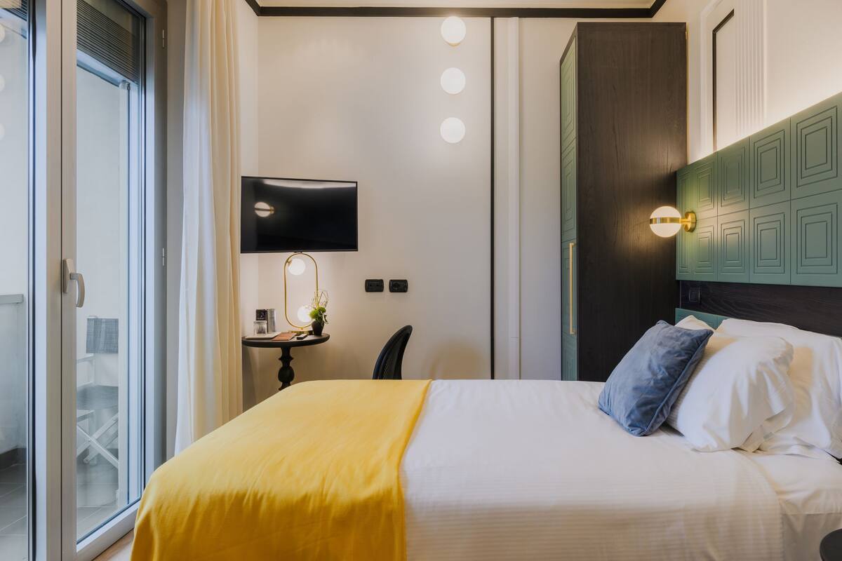 Une chambre d’hôtel avec un lit, une télévision, un bureau avec une lampe et une fenêtre.
