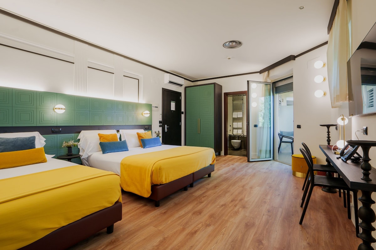 A hotel room with two beds, a dining table, and a bathroom with a glass door.