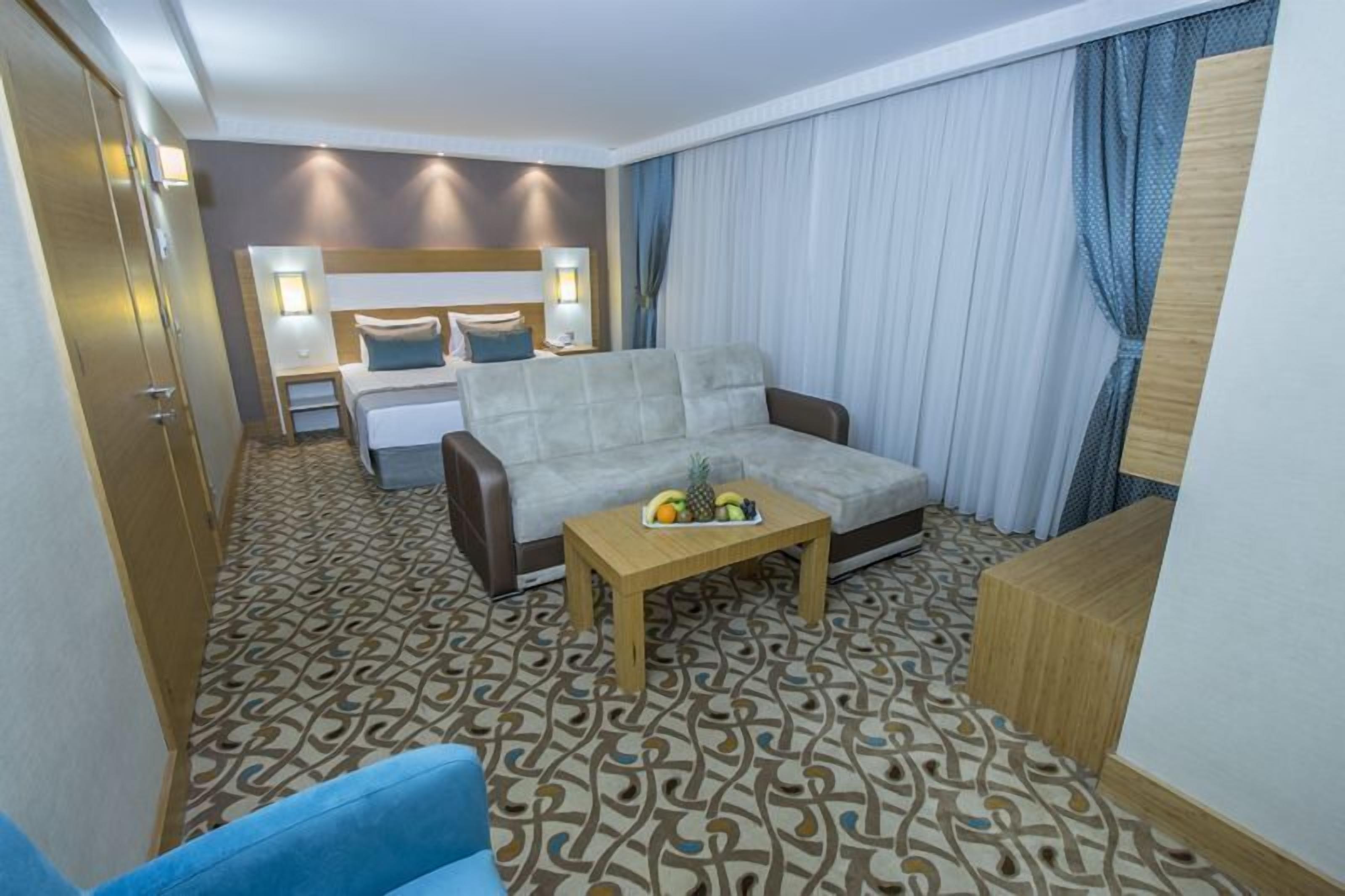Ein Hotelzimmer mit Bett, Sofa, Couchtisch mit Obst, Nachttisch und einem gemusterten Teppich.
