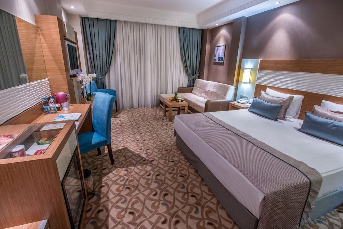 Ein Hotelzimmer mit Bett, Schreibtisch mit Stuhl, Sofa, kleinem Tisch mit Lampe und Fernseher.